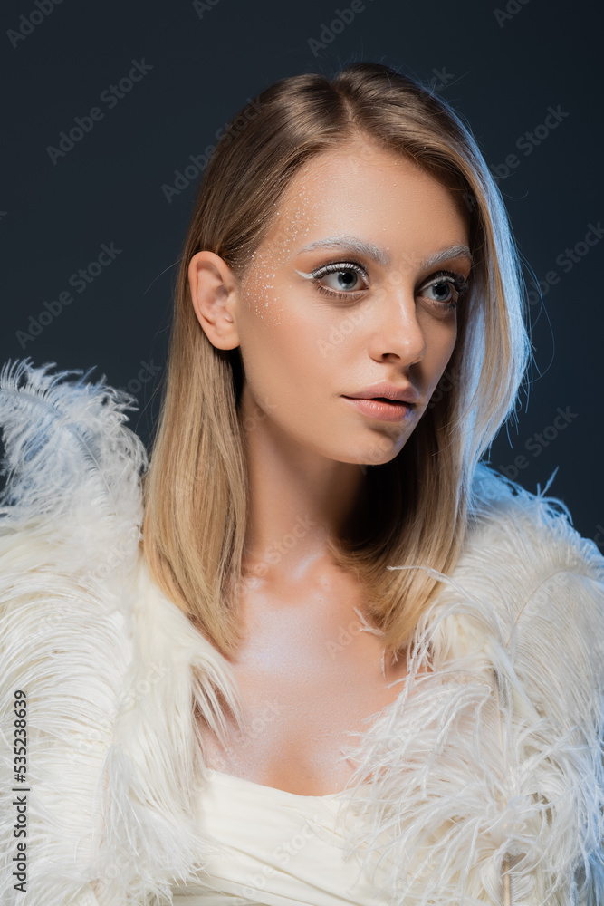 young woman in faux fur jacket with white feathers looking away isolated on blue. young woman in faux fur jacket with white feathers looking away isolated on blue.