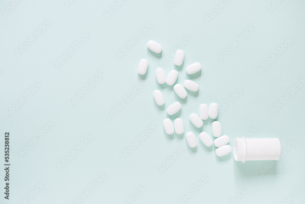  white pills and a plastic container on a blue background. Medical theme.	