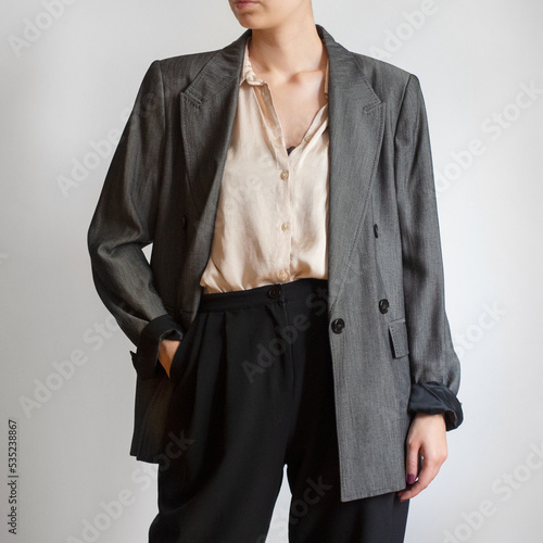 Woman wearing oversized grey blazer, elegant shirt and black trousers isolated on white background