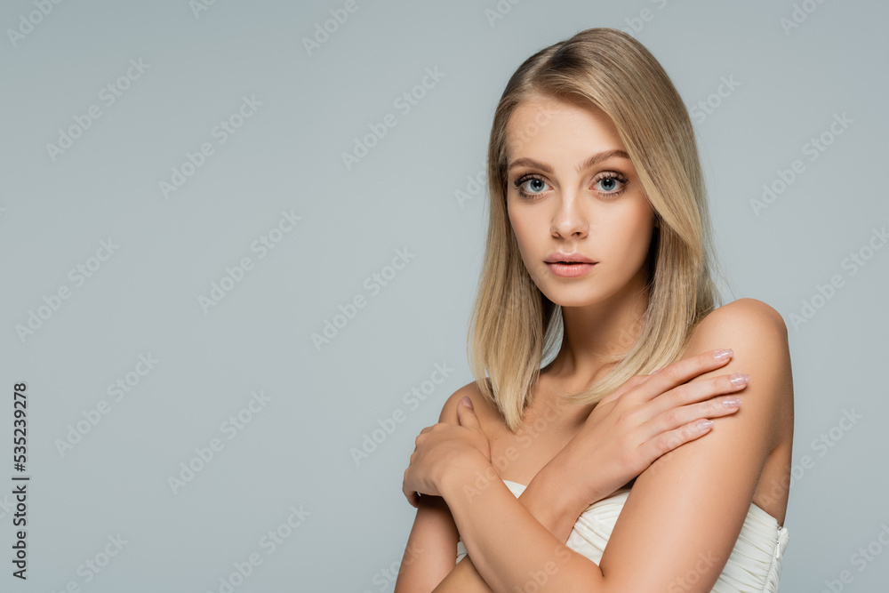 young blonde woman with bare shoulders and natural makeup posing with crossed arms isolated on grey. young blonde woman with bare shoulders and natural makeup posing with crossed arms isolated on grey.