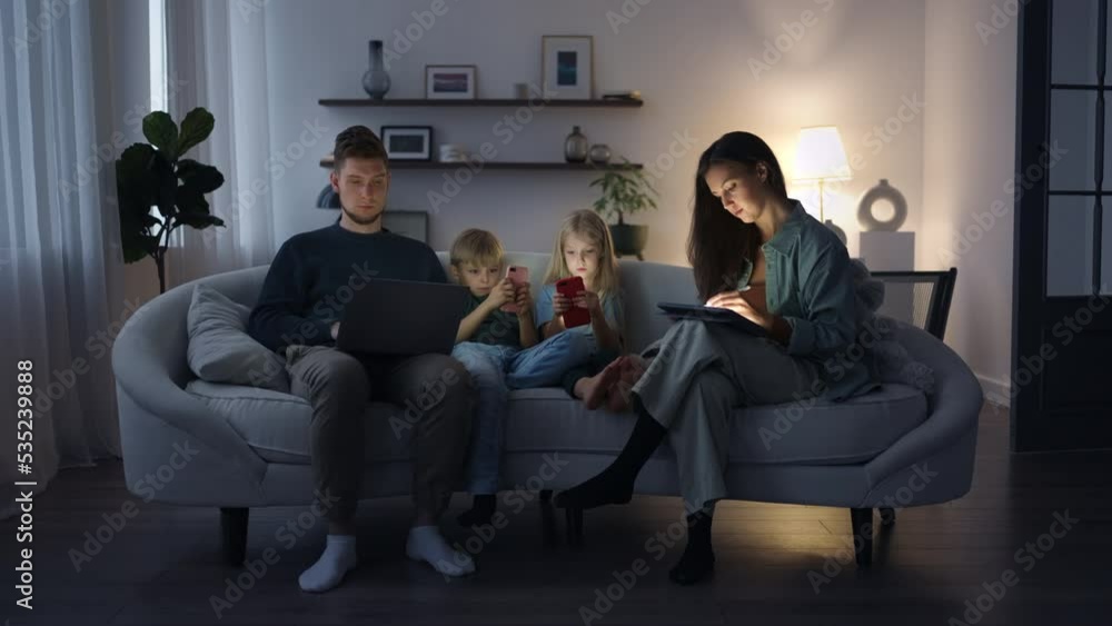 A modern family in the evening sitting on the couch uses gadgets. Electronic smartphone addiction, children and parents watch social networks and play in gadgets A modern family in the evening sitting on the couch uses gadgets. Electronic smartphone addiction, children and parents watch social networks and play in gadgets