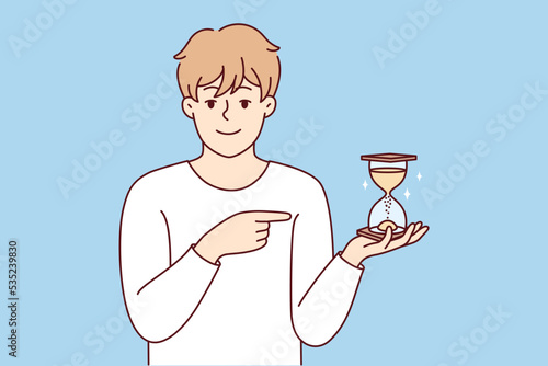 Smiling young man point at sandglass show sand flowing and time passing. Happy male show with finger and hourglass. Vector illustration. 