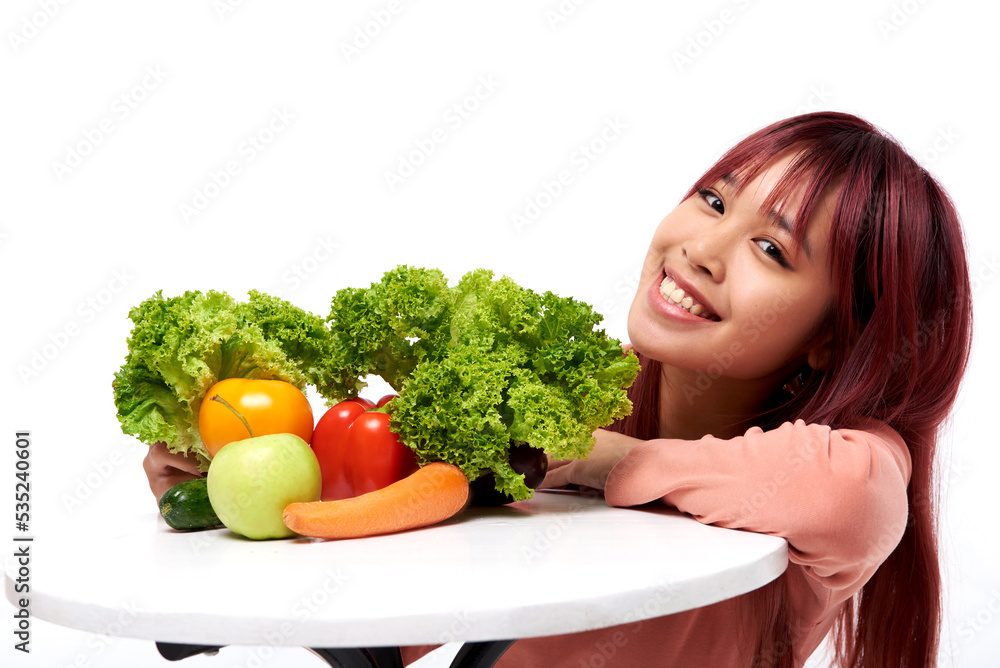 Young pretty smiling Asian girl near table with vegetables. Healthy food and diet concept. Isolated on white background. Nutrition. Natural and meal Young pretty smiling Asian girl near table with vegetables. Healthy food and diet concept. Isolated on white background. Nutrition. Natural and meal