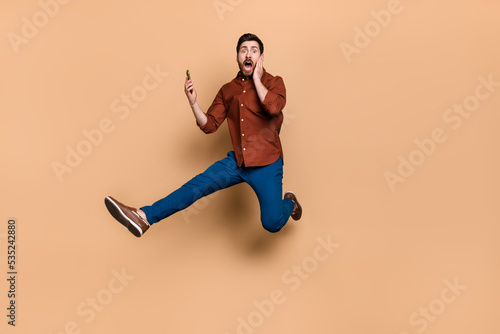 Full body portrait of impressed person arm touch cheek jumping unbelievable isolated on beige color background