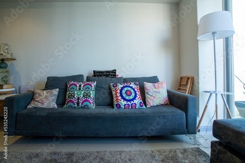 gray fabric armchair, living room with television, wooden furniture and gray carpet, mexican decoration cushions, cushions and lamp