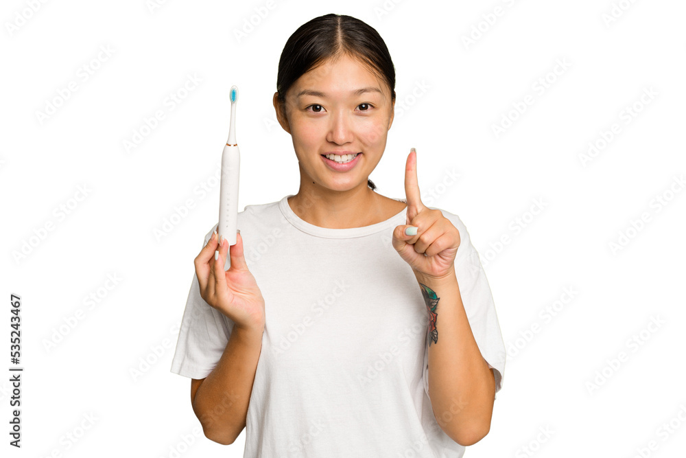 Young Asian woman holding an electric toothbrush isolated on green chroma background showing number one with finger.