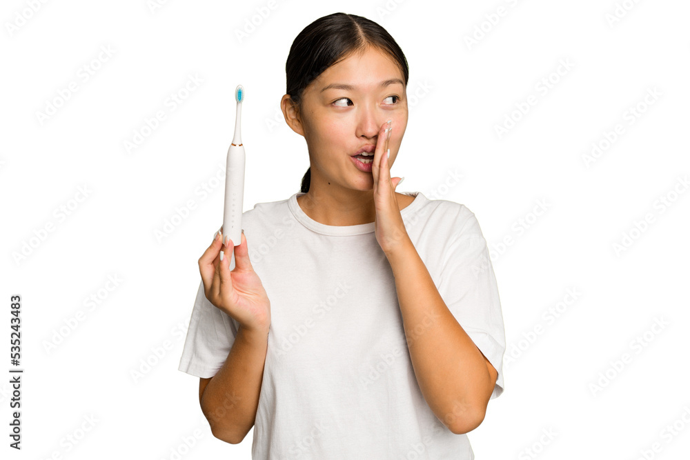 Young Asian woman holding an electric toothbrush isolated on green chroma background is saying a secret hot braking news and looking aside Young Asian woman holding an electric toothbrush isolated on green chroma background is saying a secret hot braking news and looking aside