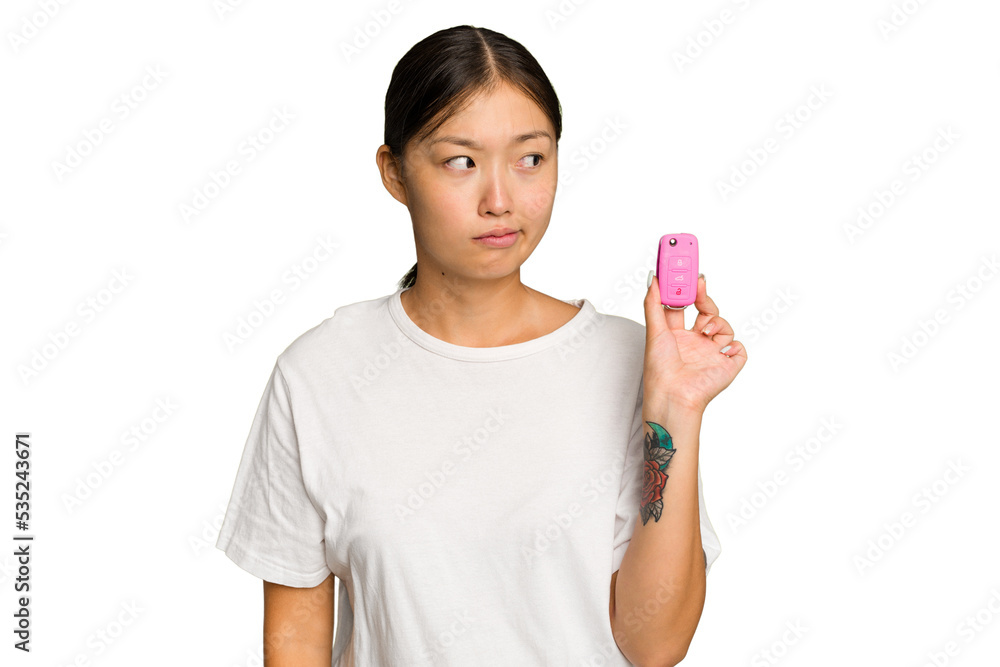 Young asian woman holding car keys isolated on green chroma background confused, feels doubtful and unsure. Young asian woman holding car keys isolated on green chroma background confused, feels doubtful and unsure.
