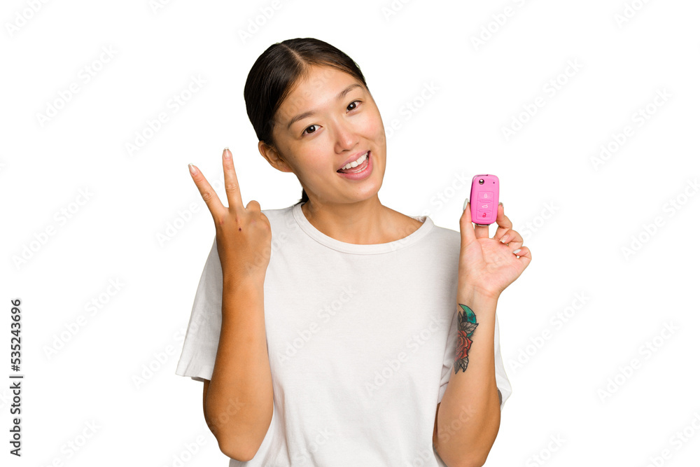 Young asian woman holding car keys isolated on green chroma background joyful and carefree showing a peace symbol with fingers. Young asian woman holding car keys isolated on green chroma background joyful and carefree showing a peace symbol with fingers.