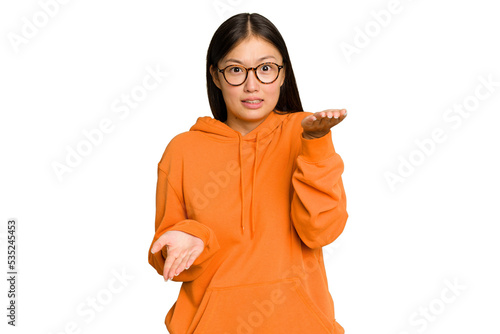 Young Asian woman isolated on green chroma background makes scale with arms, feels happy and confident.