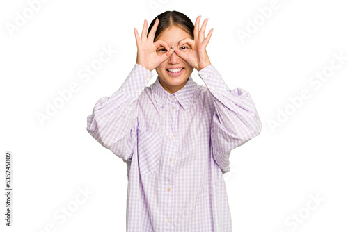 Young Asian woman isolated on green chroma background excited keeping ok gesture on eye.