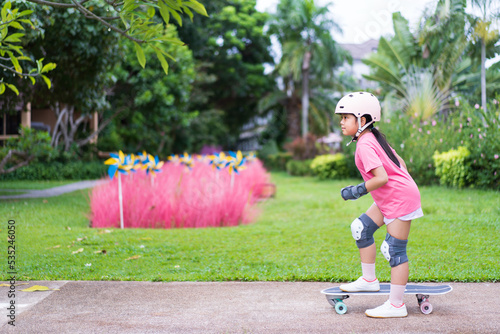 asian child or kid girl fun playing surf skate or ride skateboard in skatepark and extreme sports exercise to wearing helmet wrist knee support for body safety protect on nature lavender fields garden