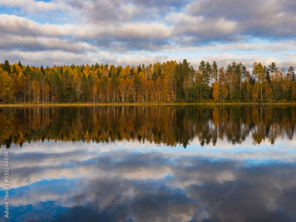 Golden autumn in Karelia, northwest Russia. Trees with yellow leaves, calm on the lake. Clouds in the sky.