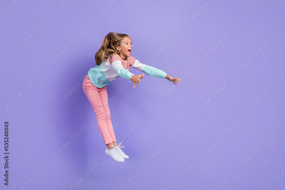 Full length photo of excited shocked small girl wear sweatshirt jumping high empty space isolated violet color background