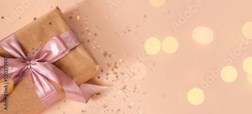 Valentines Day, Birthday or New Year present in kraft paper with pink ribbon on soft beige background with glitter and bokeh. Happy holidays celebration and giving love concept. 2022 2023 Xmas, top 
