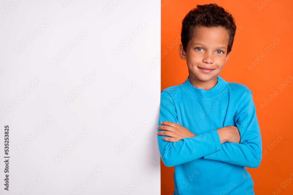 Photo portrait of charming little schoolboy folded arms white blank advert wall wear trendy blue look isolated on orange color background Photo portrait of charming little schoolboy folded arms white blank advert wall wear trendy blue look isolated on orange color background