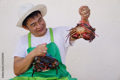 Happy handsome Asian man seafood merchant wears white hat, green appron, shows crabs. Concept : owner small business. Local food products.     photo