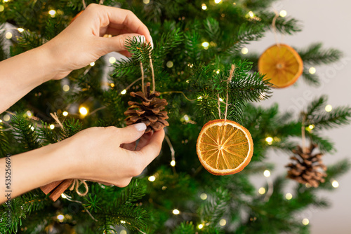 Female hands hanging handmade decoration on Christmas tree. Sustainable Christmas, zero waste, eco friendly.