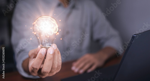 The hand of a man with a light bulb and there is a brain icon in it and he is using a notebook computer. the idea of ​​inspiration from online technology. different ideas and innovation idea concept.