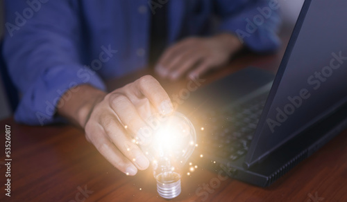 The hand of a man with a light bulb and he is using a notebook computer. Thinking differently creates inspiration and ideas.New innovations and technologies can always come from creative.