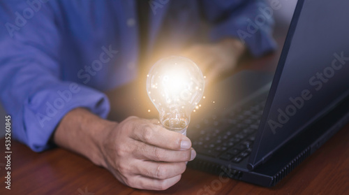 The hand of a man with a light bulb and he is using a notebook computer. Thinking differently creates inspiration and ideas.New innovations and technologies can always come from creative.