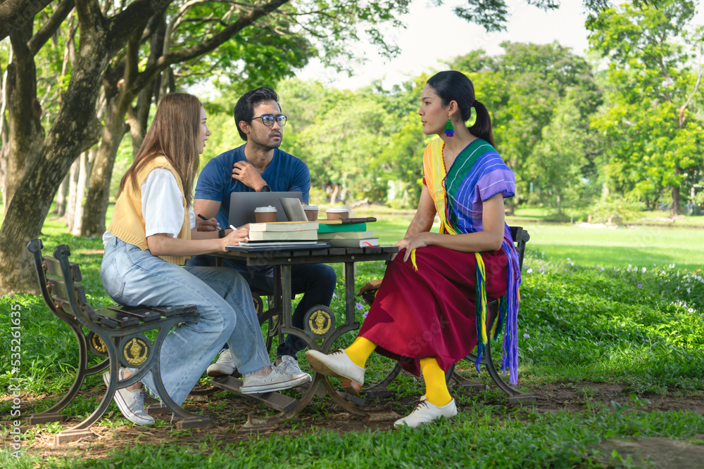 group of friends studying outdoor in the park on weekend, selective focus at a man, young asian people chatting together, there are device for learning on table such as laptop,the books,coffee cups group of friends studying outdoor in the park on weekend, selective focus at a man, young asian people chatting together, there are device for learning on table such as laptop,the books,coffee cups