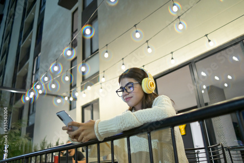young woman listens to music from her smartphone in an urban background with blurred night light photo