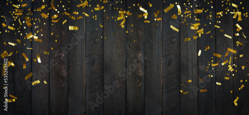 Golden glittering confetti on dark wooden planks.Top view on rustic wood surface with confetti frame.  © gudrun