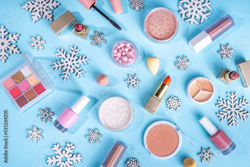 Winter make up set on light blue background, with artificial snowflakes and Christmas tree branches. Various makeup professional cosmetics - shadows, lipstick, mascara, blush. Christmas beauty sale