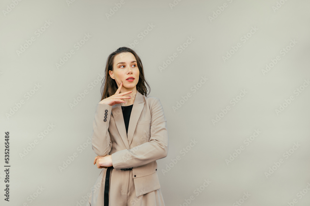 Portrait of a pensive female worker in a beige suit standing on a beige background, looking away and thinking. Copy space Portrait of a pensive female worker in a beige suit standing on a beige background, looking away and thinking. Copy space