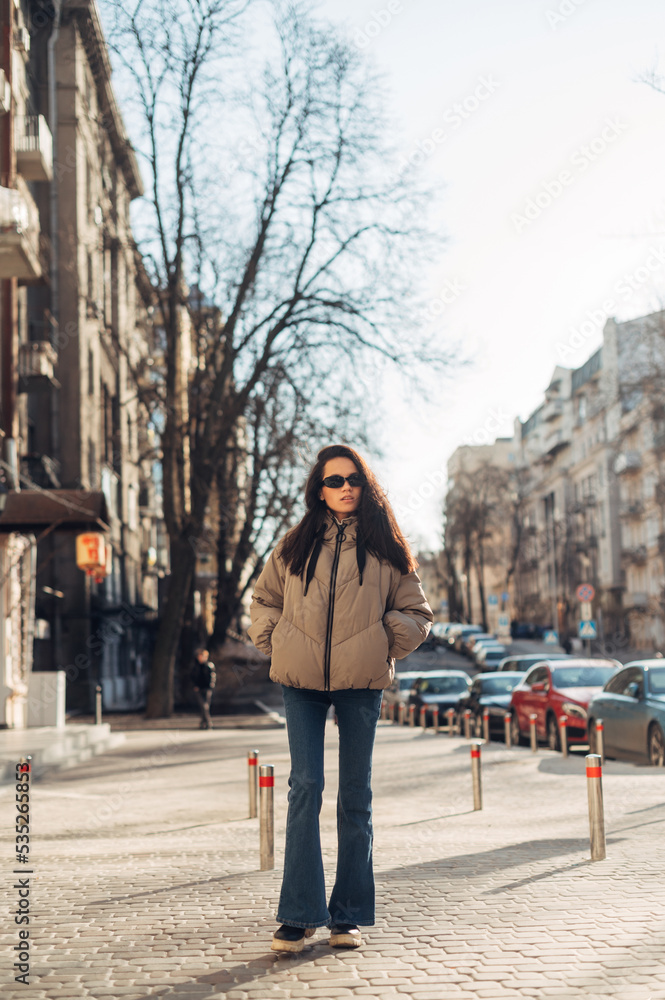 Stylish woman in casual clothes walking down the street on a spring sunny day, full length portrait.