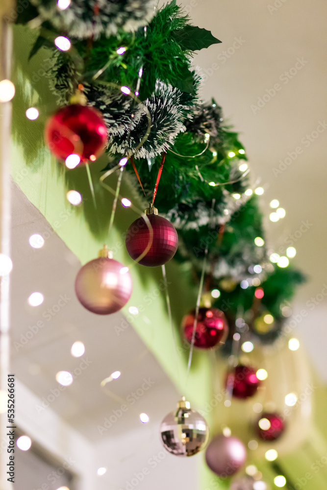 Christmas decor above the window. Green garland and balls of red and pink color