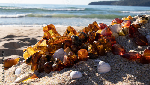 Dark orange Baltic amber beads and shells on the sand. Amber jewelry near the sea. Slavic culture.