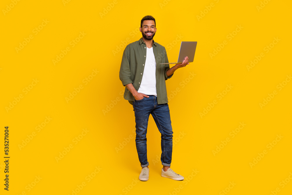 Full length photo of funky handsome man wear khaki shirt typing modern device isolated yellow color background Full length photo of funky handsome man wear khaki shirt typing modern device isolated yellow color background