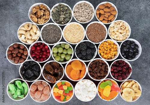 Berries, nuts, seeds, dried fruits in round containers. Background with a mix of healthy snacks. Assorted vitamin food on a grey background.