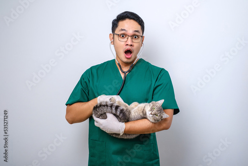 Shocked doctor in vet clinic examining cat with stethoscope, gasping amazed while holding cat in his arm