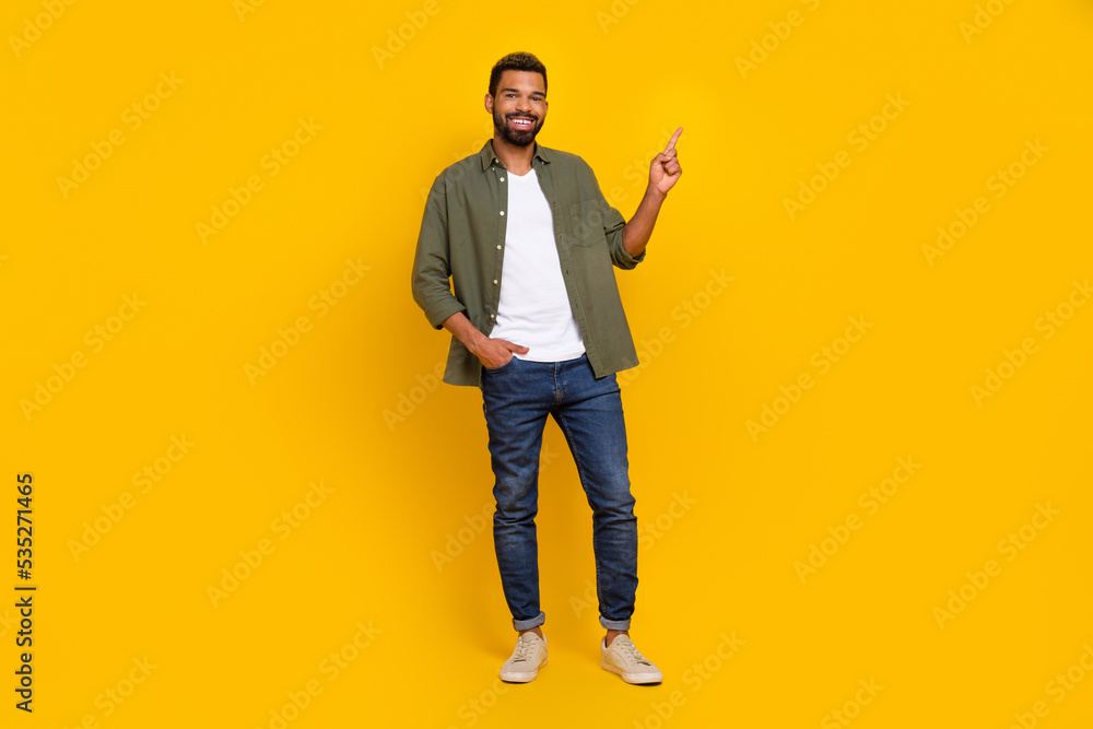 Full length photo of confident funky man wear khaki shirt pointing empty space isolated yellow color background Full length photo of confident funky man wear khaki shirt pointing empty space isolated yellow color background