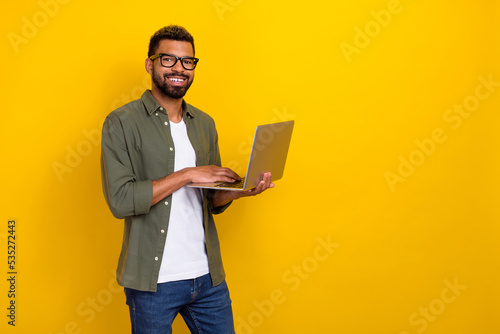 Photo of pretty confident man wear khaki shirt spectacles typing modern device empty space isolated yellow color background