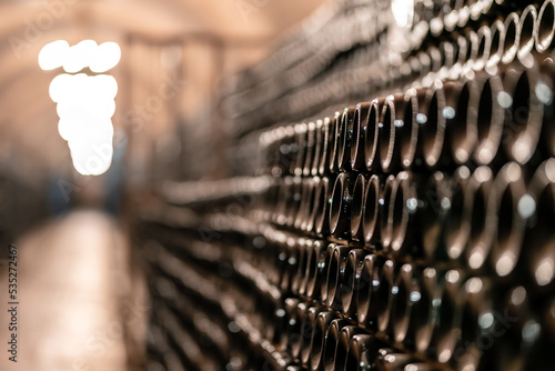 Glass wine bottles stacked in rows at winery storehouse. Wine-making produce storage at winery cellar. Wine cellar interior view. Wine making concept.