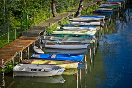 small colorful boats moored in a row at the pier in the river channel. in the background trees and plants
