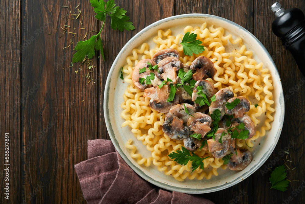 Fusilli pasta with mushrooms, cheese and garlic creamy sauce on plate on old wooden dark table background. Top view. Traditional Italian cuisine. Fusilli pasta with mushrooms, cheese and garlic creamy sauce on plate on old wooden dark table background. Top view. Traditional Italian cuisine.