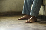 Close up on a male bare feet on the hard wood floor while sitting on the sofa in semi light room wearing denim jeans. Man bare feet on the floor. No face visible