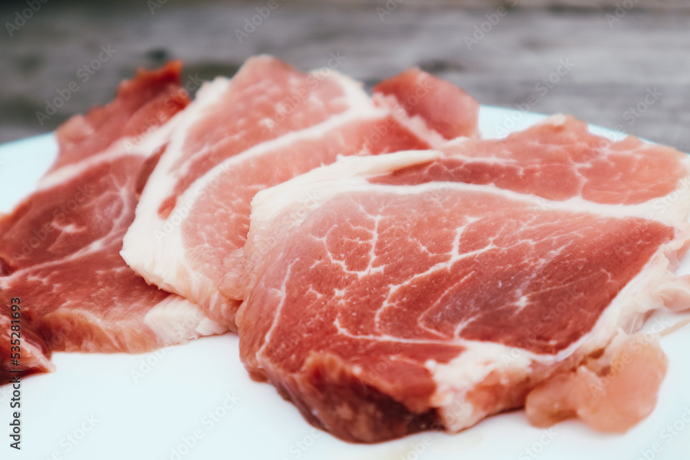 High Angle View Of Slised Meat In White Plate On Table. Fresh steak in plate. Uncooked raw pork meat slices on a white plate and wooden table.