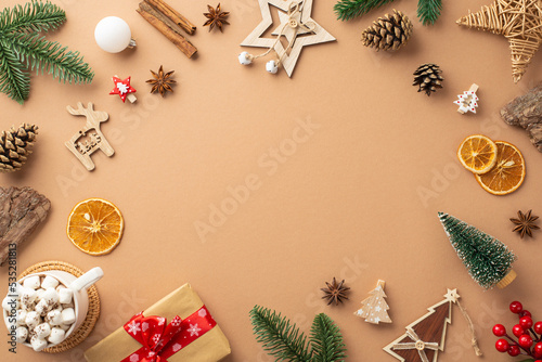 Top view photo of christmas decorations wood ornaments giftbox cup of cocoa mistletoe pine cones branches bark cinnamon dried orange slices on isolated beige background with copyspace in the middle