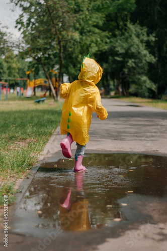 Fototapeta Naklejka Na Ścianę i Meble -  Girl in a yellow dress with an umbrella joyful spring runs through the puddles on a rainy day