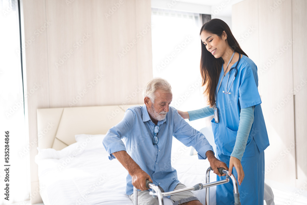 Portrait of Asian young nurse helping old elderly disable man grandfather to walk by using walker equipment in the bedroom. Senior patient of nursing home moving with walking frame and nurse support Portrait of Asian young nurse helping old elderly disable man grandfather to walk by using walker equipment in the bedroom. Senior patient of nursing home moving with walking frame and nurse support