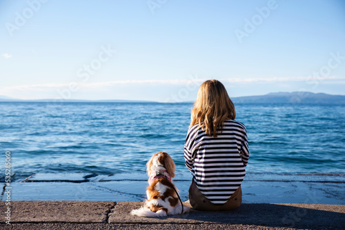 Rear view shot of woman sitting with dog on jetty