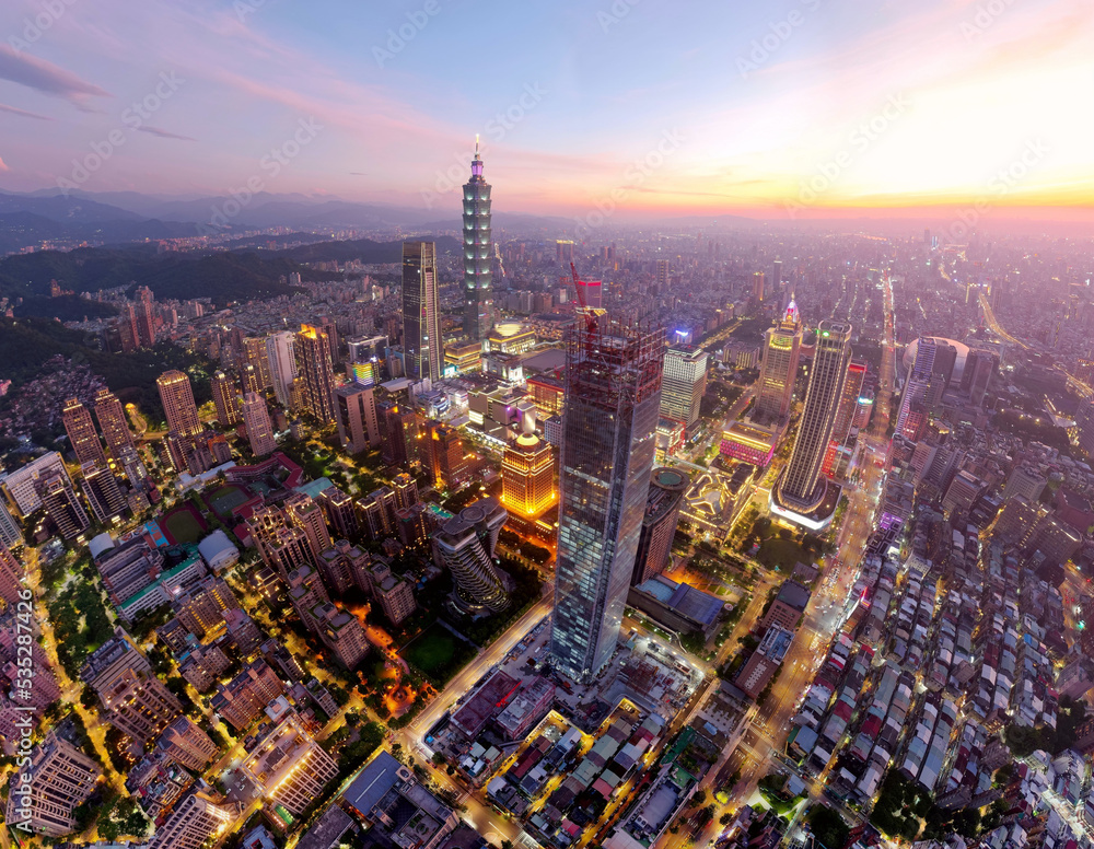 Obraz premium Aerial view of Downtown Taipei at dusk, the vibrant capital city of Taiwan, with 101 Tower standing among modern skyscrapers in Xinyi District and city lights dazzling under dramatic twilight sky