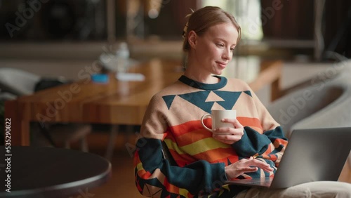 Happy blonde woman working on laptop and drinking coffee in cafe