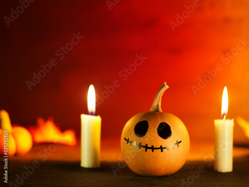 Halloween background  pumpkin with painted face. Red background  burning candles and knitted little pumpkins. Copy space